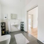 Badezimmer mit Toilette, Waschbecken und Dusche. Blick in das Wohnzimmer.