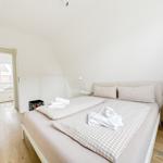 Schlafzimmer mit Doppelbett, weißen Wänden und Holzboden. Durchgang zu einem Fensterbereich.