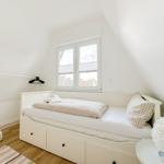 Schlafzimmer mit weißem Bett, Fenster und Kleiderständer.