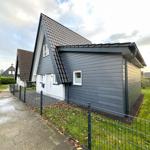 Moderne Villa mit grauer Fassade und weißer Tür. Grünfläche und Zaun sind sichtbar.