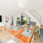 Essbereich mit Holztisch, Stühlen und Blumen. Küche, Wohnbereich und Treppe sind sichtbar.