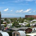 Panorama mit Campingplatz, Bäumen und Meer unter blauem Himmel mit weißen Wolken.