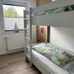 Zimmer mit Doppelstockbett, Fenster und Holzschrank.
