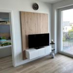 Wohnzimmer mit TV, Holzwand und Balkonzugang. Nebenraum mit Bett sichtbar.