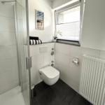 Badezimmer mit Dusche, Toilette und Fenster mit Jalousie.
