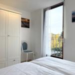 Bedroom with white wardrobe, chair, and balcony view.