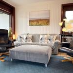 A living room with a gray sofa, two black chairs, and a wall picture.