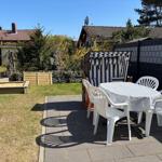 Backyard with table, chairs, and beach chair. Garden area with sandbox and fence.