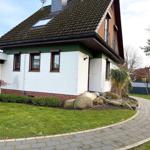 House with white facade, green roof, and landscaped garden with stone path.