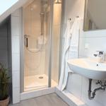Bathroom with shower, sink, and mirror. White tiles and towel rack.