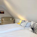 A bedroom with a double bed, sofa, and nightstand under a sloped ceiling.