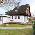 House with white facade, green roof, and garden with stones and trees.