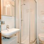 Badezimmer mit Dusche, Waschbecken und Toilette. Fliesenwand und Holztür.