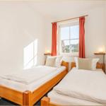 Zwei Einzelbetten mit weißen Bettwäschen und Holzrahmen. Fenster mit roten Vorhängen.