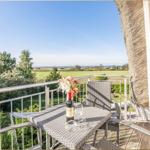 Terrasse mit Tisch, Stühlen und Weinkrug. Blick auf grüne Wiesen und Bäume.