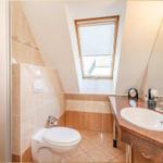 Badezimmer mit Toilette, Waschbecken und Dachfenster. Fliesenwand und Boden.