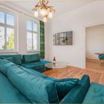 Wohnzimmer mit tiefblauem Sofa, Holzboden und grünen Vorhängen. Anblick auf die Straße durch Fenster.