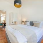 Schlafzimmer mit Doppelbett, Spiegelschrank und Holzboden. Durchgang zu Essbereich mit Tisch und Stuhl.