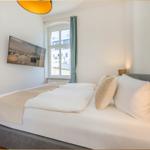 Schlafzimmer mit Bett, Fenster und Wandbild. Holzboden und moderne Beleuchtung.