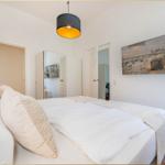 Schlafzimmer mit Bett, Wandbild und Deckenleuchte.