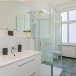 Badezimmer mit Dusche, Waschbecken und Toilette. Fenster sorgt für Tageslicht.