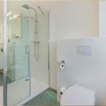 Duschkabine mit Glaswand, Toilette und Toilettenpapierhalter an der Wand.