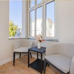 Zwei Sessel und ein Tisch stehen vor großen Fenstern mit Blick auf Gebäude.