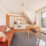 Wohn- und Küchenbereich mit Sofa, Esstisch und Balkonzugang.