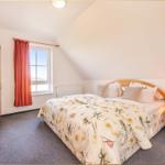 Schlafzimmer mit Dachschrägen, Bett, Kleiderschrank und Fenster mit roten Vorhängen.