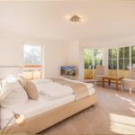 Schlafzimmer mit Doppelbett, TV und Sitzgelegenheit an großen Fenstern.