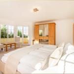 Schlafzimmer mit Doppelbett, Kleiderschrank und Sitzbereich mit Blick auf Garten.