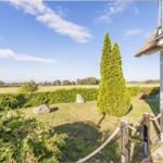 Haus mit Blick auf grüne Wiesen und Bäume. Garten mit Hecke, Zypressen und Stein.