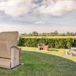Garten mit Rattanliege, Grill und Steinbank. Blick auf Feld und Hecke.
