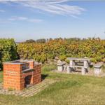 Roter Backstein-Grill neben Steinbank im Garten mit Hecken und Feldern im Hintergrund.