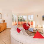 Wohnzimmer mit weißem Sofa, rotem Sessel und Glas-Tisch. Große Fenster und Wandbild.