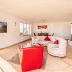 Wohnzimmer mit Sofa, Kamin und rotem Sessel. Fenster, Wandbild und Essbereich sichtbar.