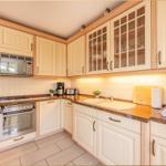 Küche mit hellen Schränken, Edelstahlgeräten und Steinarbeitsplatten.