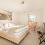 Schlafzimmer mit Bett, zwei Stühlen und Fenster. Wandbilder und Teppichboden.