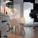 Ein Sessel mit Holzbeinen steht im Wohnbereich neben einer Küchenzeile mit Barhockern.