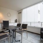 Terrasse mit Tisch, Stühlen und Sitzgelegenheit. Glaswand und Blick auf Bäume.