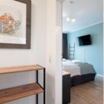 Schlafzimmer mit Bett, TV und Holzboden. An der Wand hängt ein Bild in einem Holzrahmen.