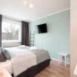 Schlafzimmer mit Bett, TV und Fenster. Holzboden und hellblaue Wand.