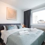 Schlafzimmer mit Bett, Nachttischen und Fenster mit Blick auf Gebäude.