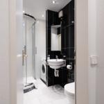 Badezimmer mit Dusche, Waschmaschine und Toilette. Schwarze und weiße Fliesen.