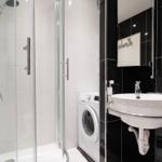 Badezimmer mit Dusche, Waschmaschine und Waschbecken.