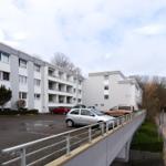 Modernes Mehrfamilienhaus mit Parkplatz und Bäumen im Hintergrund.