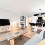 Wohnzimmer mit Sofa, Couchtisch, Fernseher und offener Küche mit Barhockern.