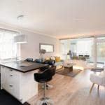 Küche mit Insel und Essbereich, Wohnzimmer mit Sofa und Balkonansicht.