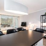 Wohn- und Essbereich mit schwarzen Stühlen, TV und Regal. Durchgang zur Terrasse.