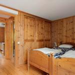Zimmer mit Holzwand und zwei Betten. Tür führt in einen weiteren Raum.